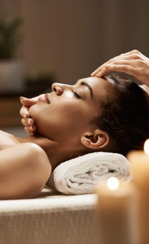Attractive african girl enjoying face massage in spa salon. Closed eyes.